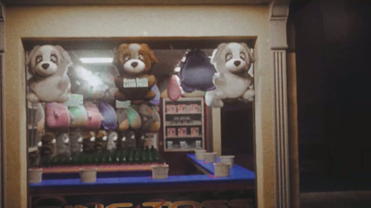 A moving camera explores a carnival ring-toss booth. Hanging plush prizes fill the upper walls, while green bottles, rings, buckets, and signs occupy the counter below.